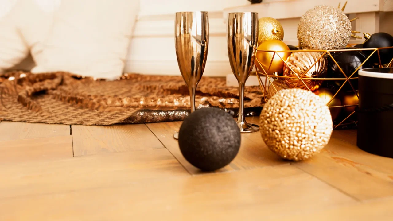 Two gold drinking glasses with disco balls and a baubles and a gold runner. Gold and black decor.