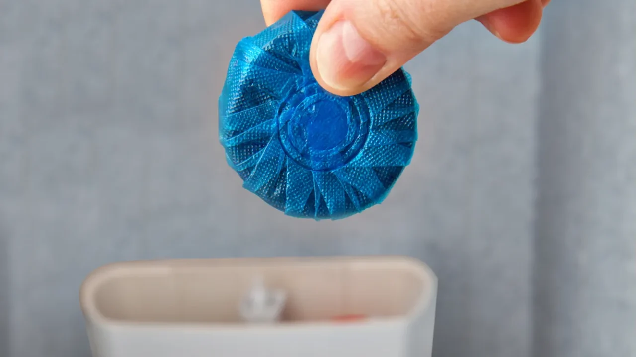 closeup of hand pushes blue cleaning tablet into drain tank