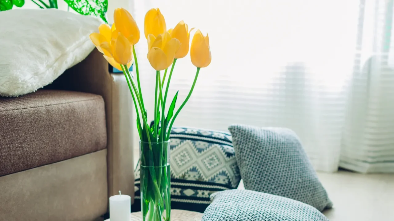 Details of modern living room interior. Yellow tulips in a clear vase and a candle. Tatami straw cushion. Light brown sofa next to the vase and a white cushion on it.