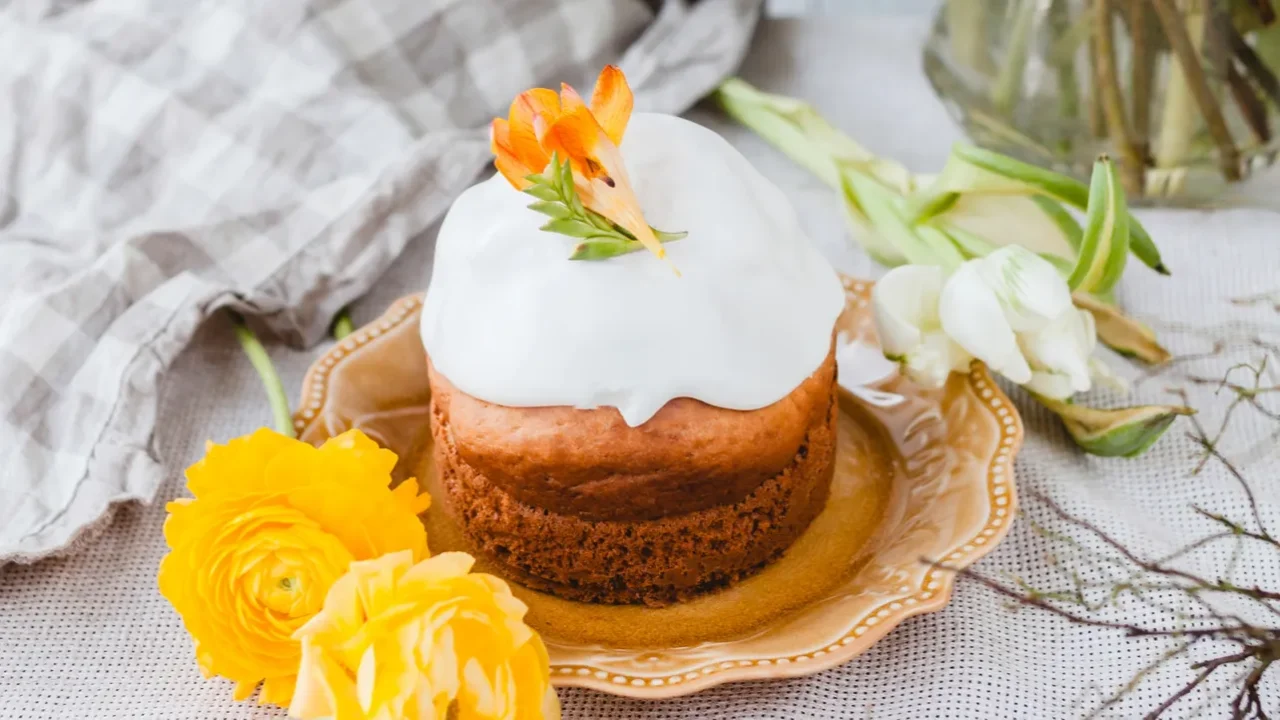 Easter cake with fresh flowers on a table and a gingham napkin. A vase of fresh flowers placed at the back.