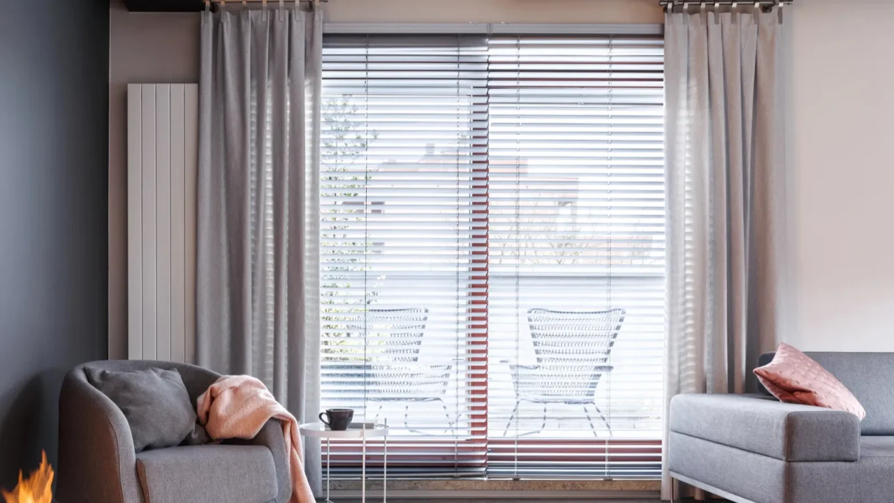 Contemporary grey apartment with blinds and curtains on windows. Grey sofa pair with cushions and a throw on it.