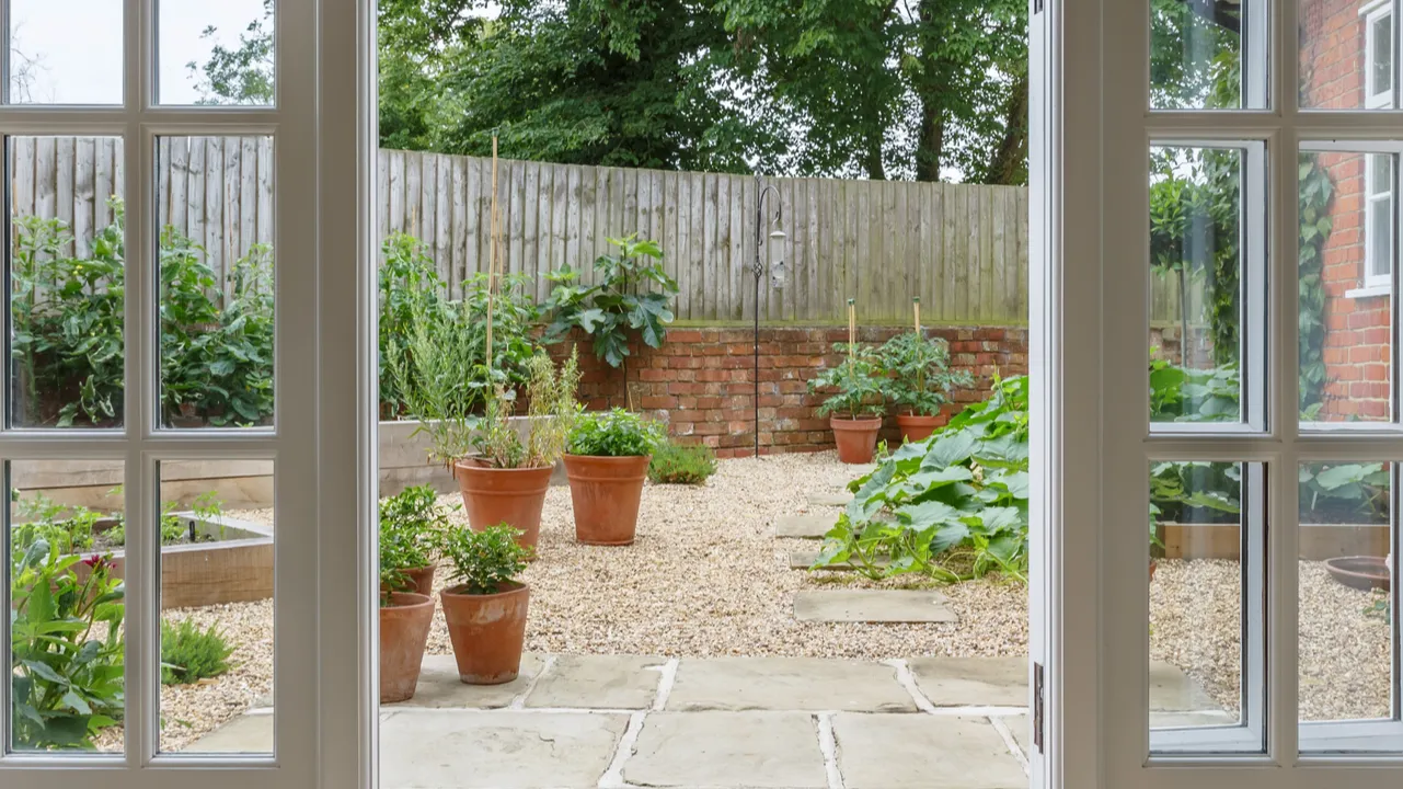 French doors leading to kitchen garden with plants in terracotta pots.