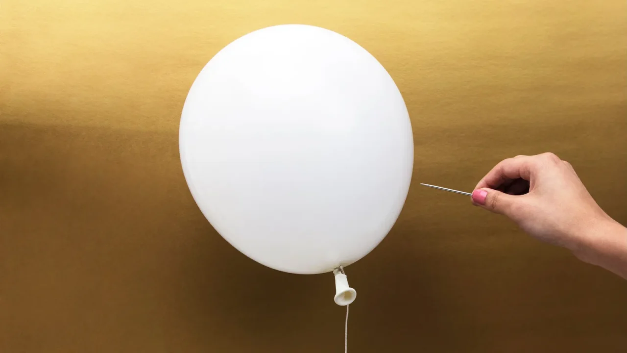 hand with pin popping a white balloon