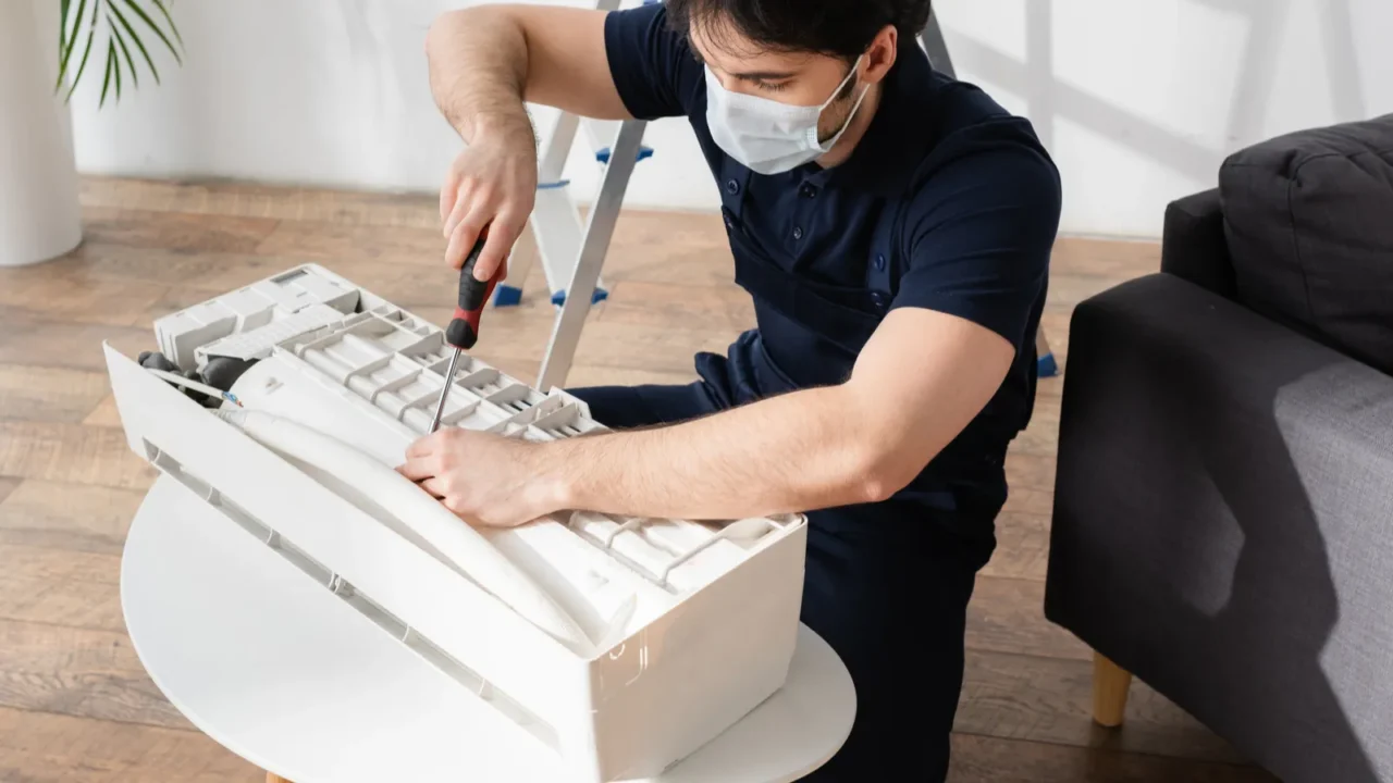 handyman in medical mask holding screwdriver while fixing broken air