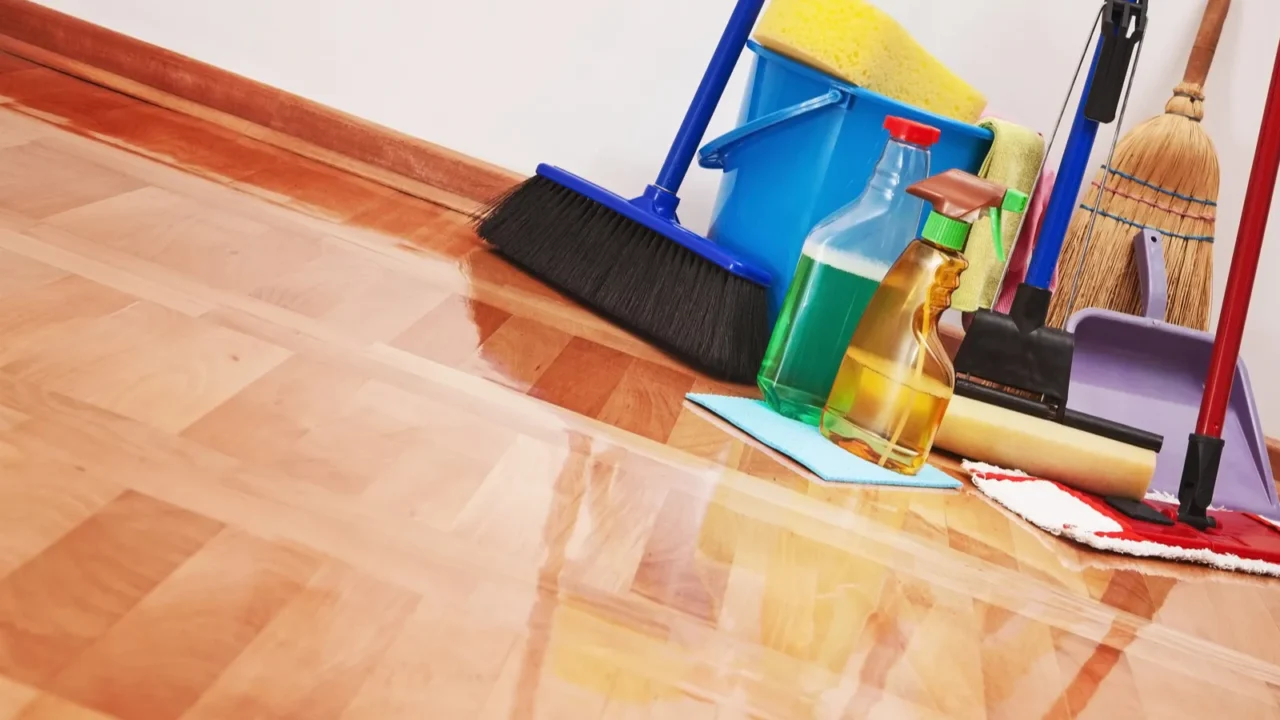 Floor cleaning supplies featuring broomsticks, mops, sponge and spray bottles are grouped together in a bunch on tile floors.