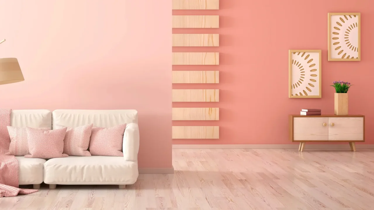 Interior design of a modern living room with pink wall. Frames above a table and a sofa with pink cushions and a throw blanket and a floor lamp.