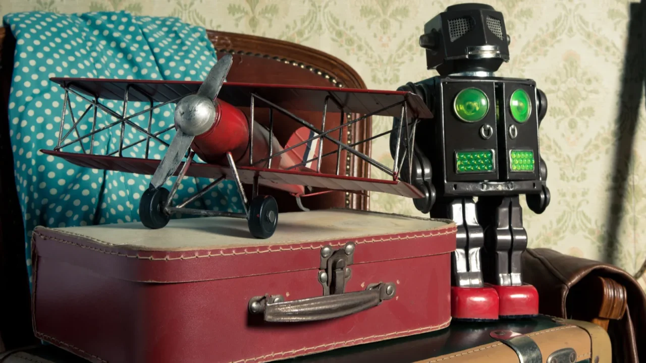 A vintage toy airplane and a retro robot toy displayed on a red suitcase with a blue polka dot cloth in the background.