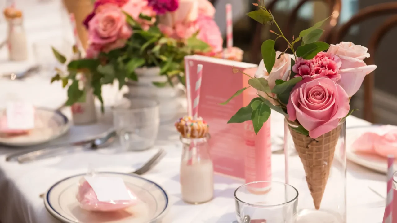 Pink flower themed setting for meal. Pink and peach flowers and setting on white tablecloth.