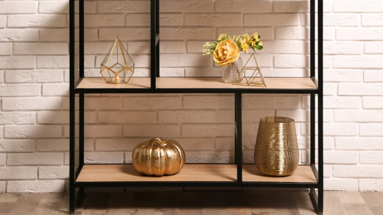 Shelving with different decor near white brick wall interior design. Golden decor and vase.