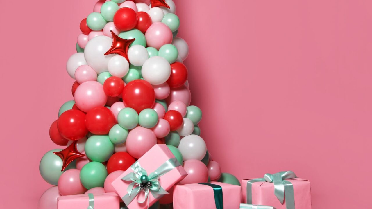 New modern concept Christmas tree made of balloons. Gift boxes below in front of a pink background.