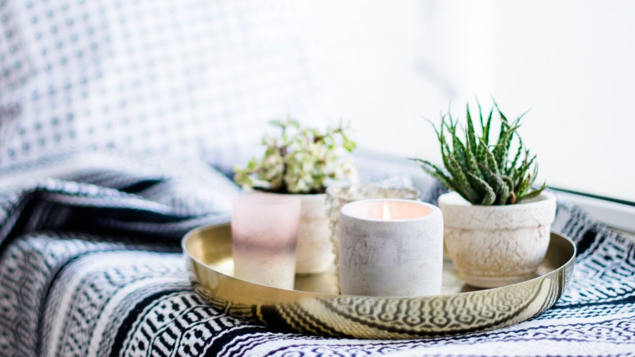 Real apartment interior decor. Aromatic candles and cactus succulent plants on vintage tray with black and white pillows and blanket on white windowsill.