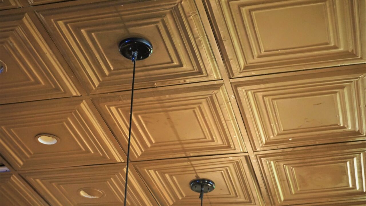 Coffered, patterned tin ceiling with recessed lights and two lighting fixtures.