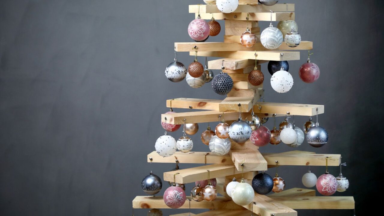 Alternative Christmas tree. Christmas tree made of wood boards, decorated with baubles in front of a gray background.