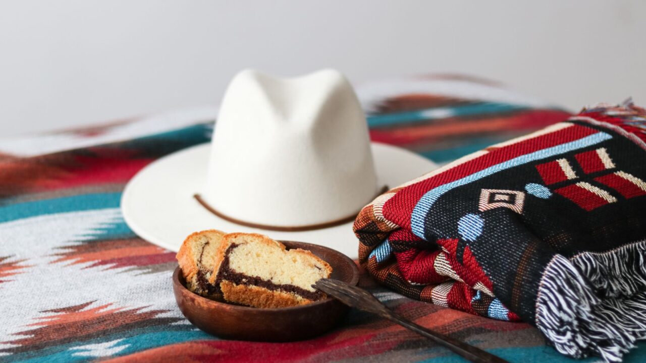 A slice of Chocolate vanilla pound cake served on wooden bowl, cotton Navajo blanket, and wool hat.