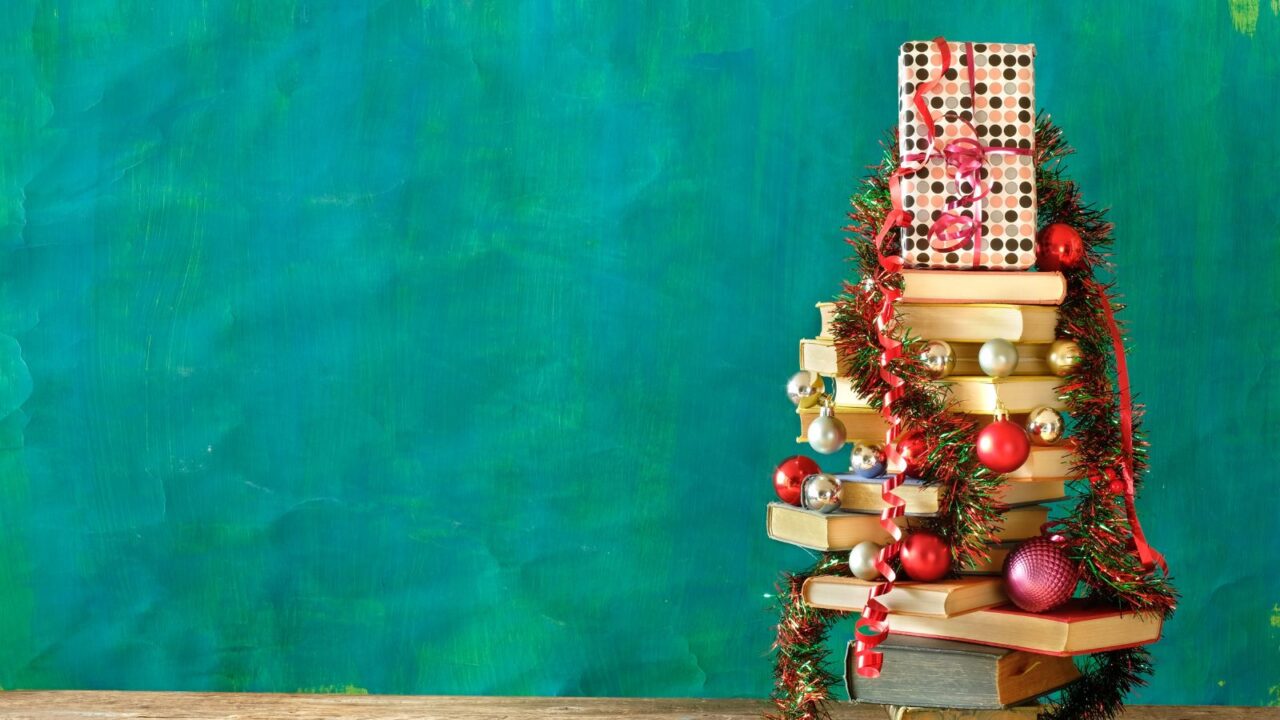 A Christmas tree made of books in front of a green wall. Baubles, ribbons, and a gift at the top. Christmas holiday concept.