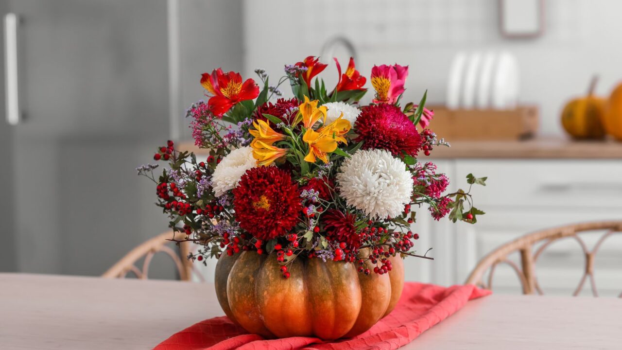 Fresh flowers in a pumpkin vase on dining table in kitchen. Red runner and rattan chairs.