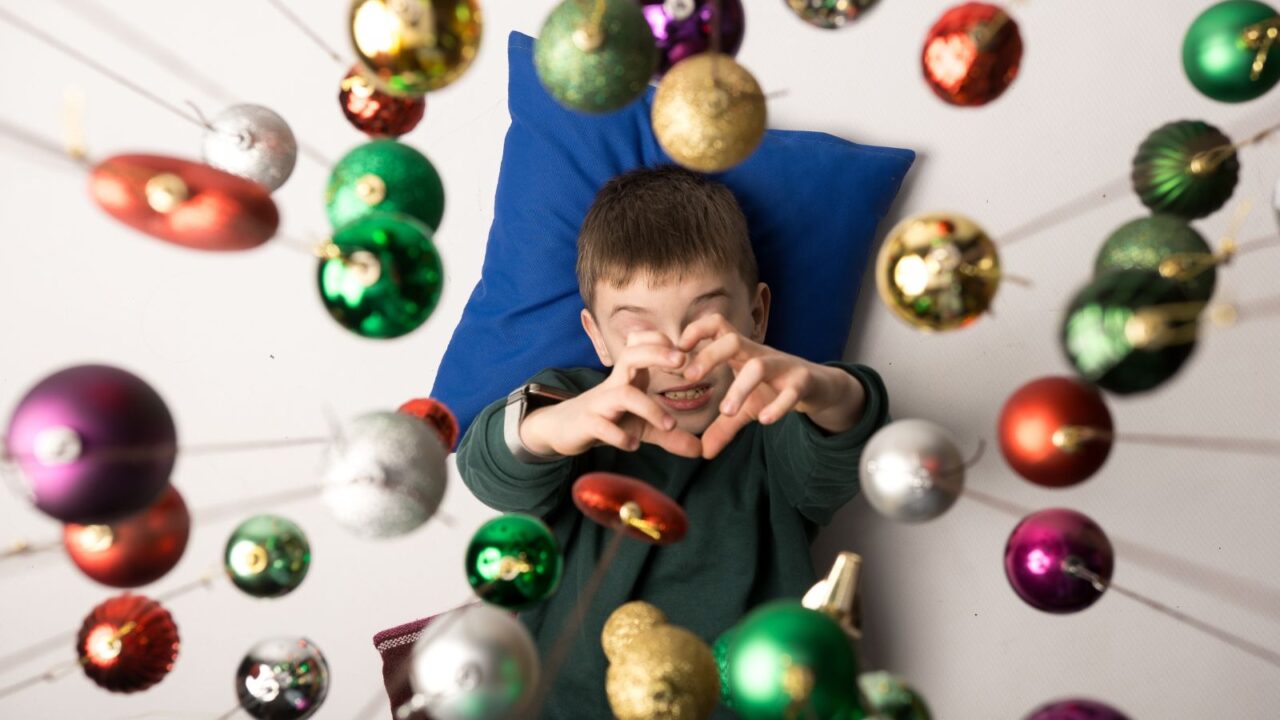 Top view of a happy child surrounded by sparkling Christmas decorations hanging from a ceiling. Captures the magic and innocence of the holiday season.