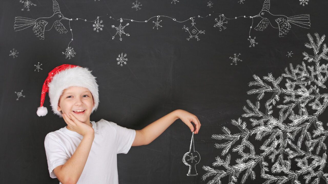 Child decorates a Christmas tree drawing on blackboard. Christmas holiday concept.