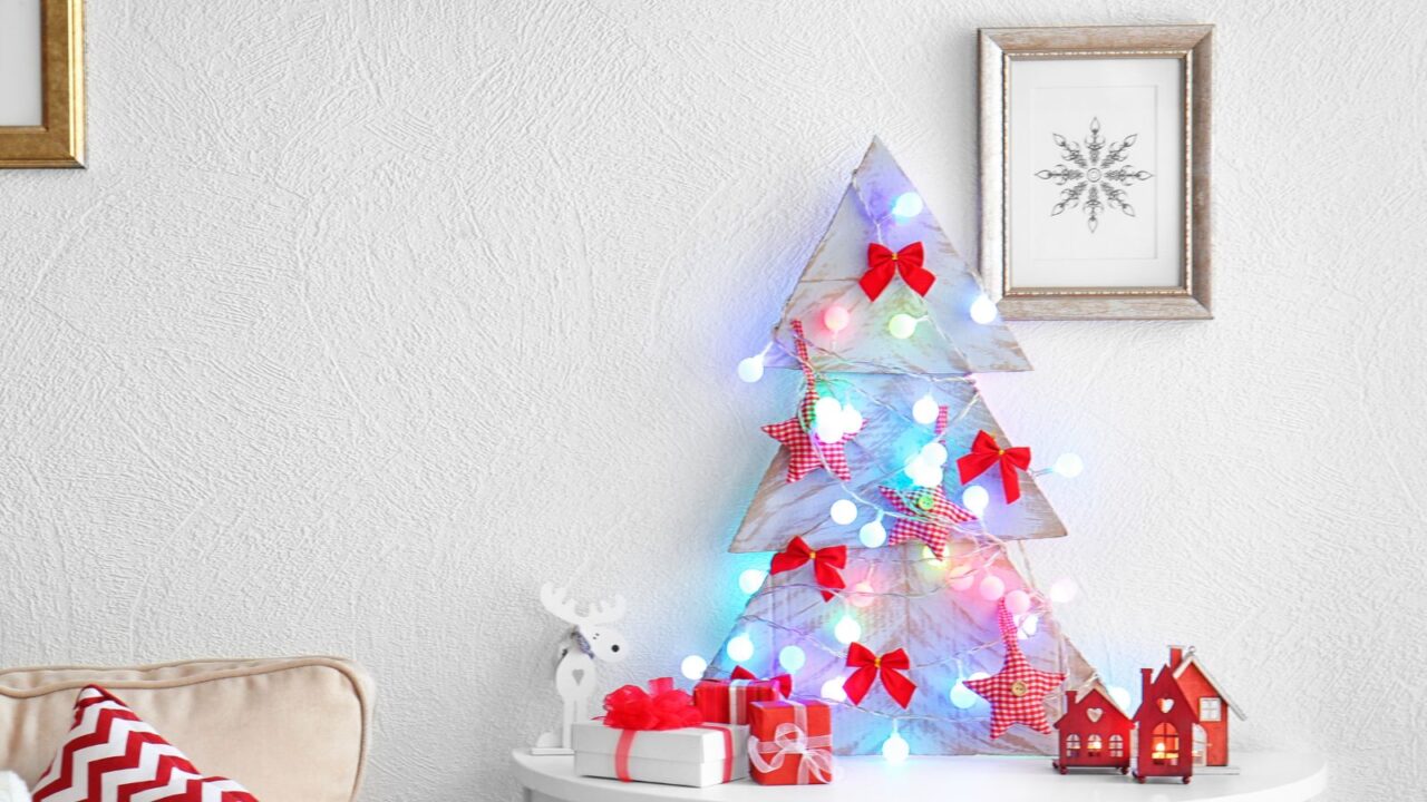 Decorated handmade Christmas tree on a white table with ribbons, lights, and stars. Christmas decor and presents on the table. A gold and silver frame hanging on the wall.