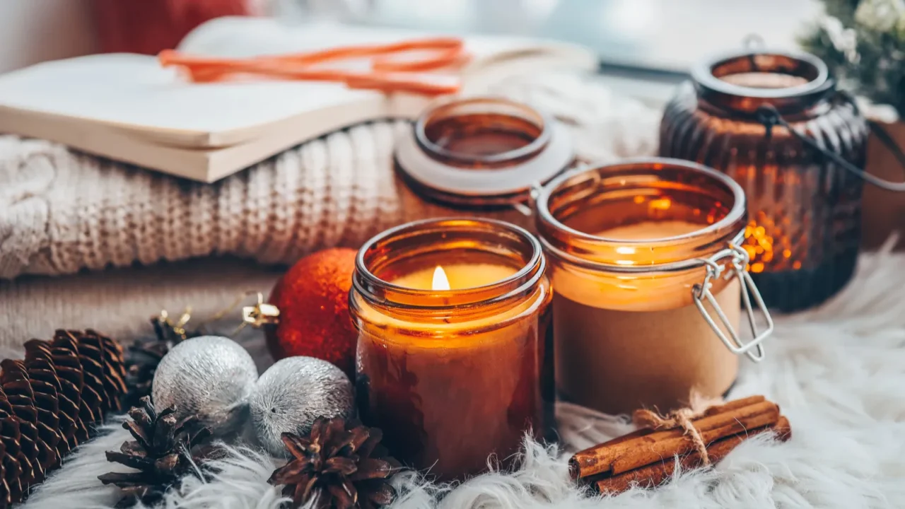 Burning scented candles in jars with cinnamon sticks bundle and Christmas ornaments around them.