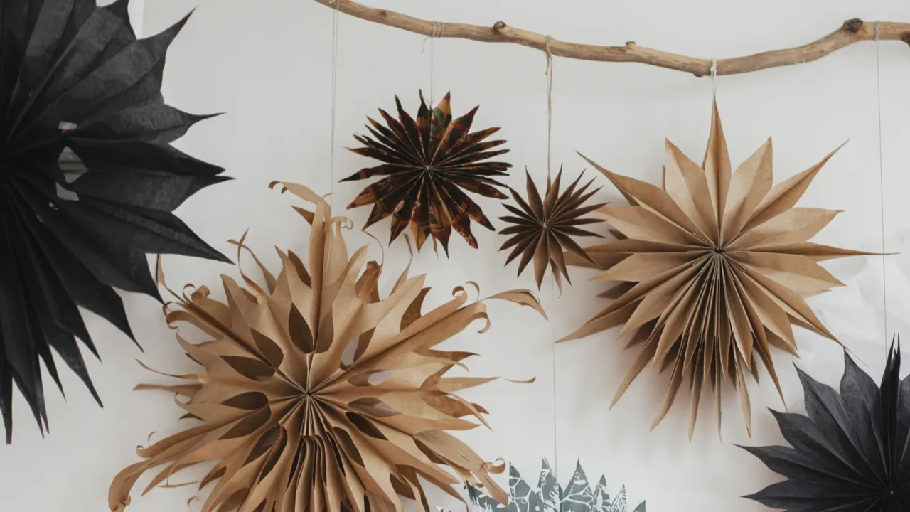 stylish christmas stars hanging from wooden branch on white wall