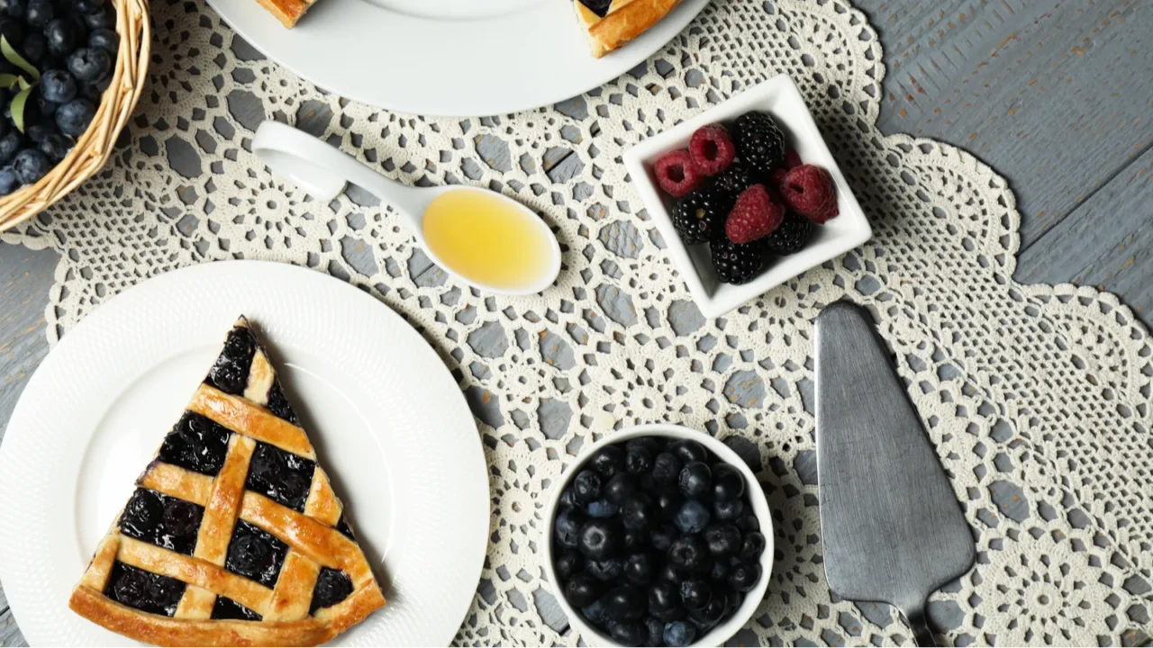 A pie with blueberries, fresh berries, honey and cake on a lace table runner.