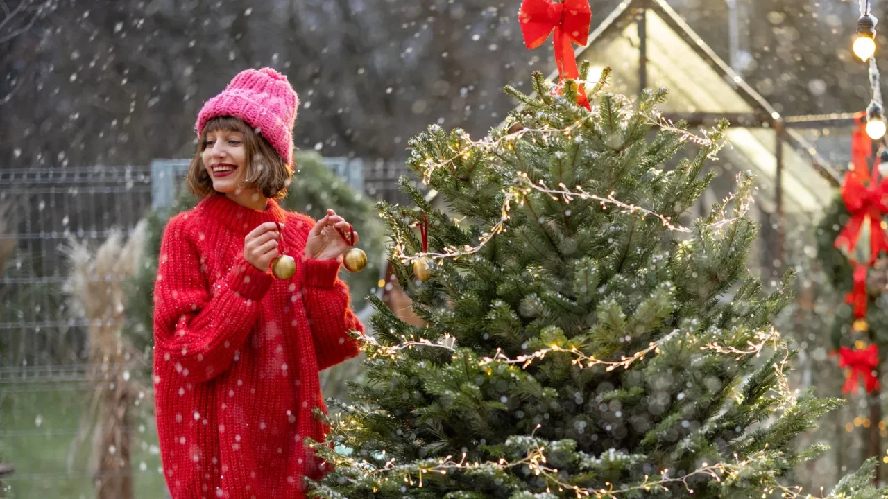 young woman in red decorates lush christmas tree with festive