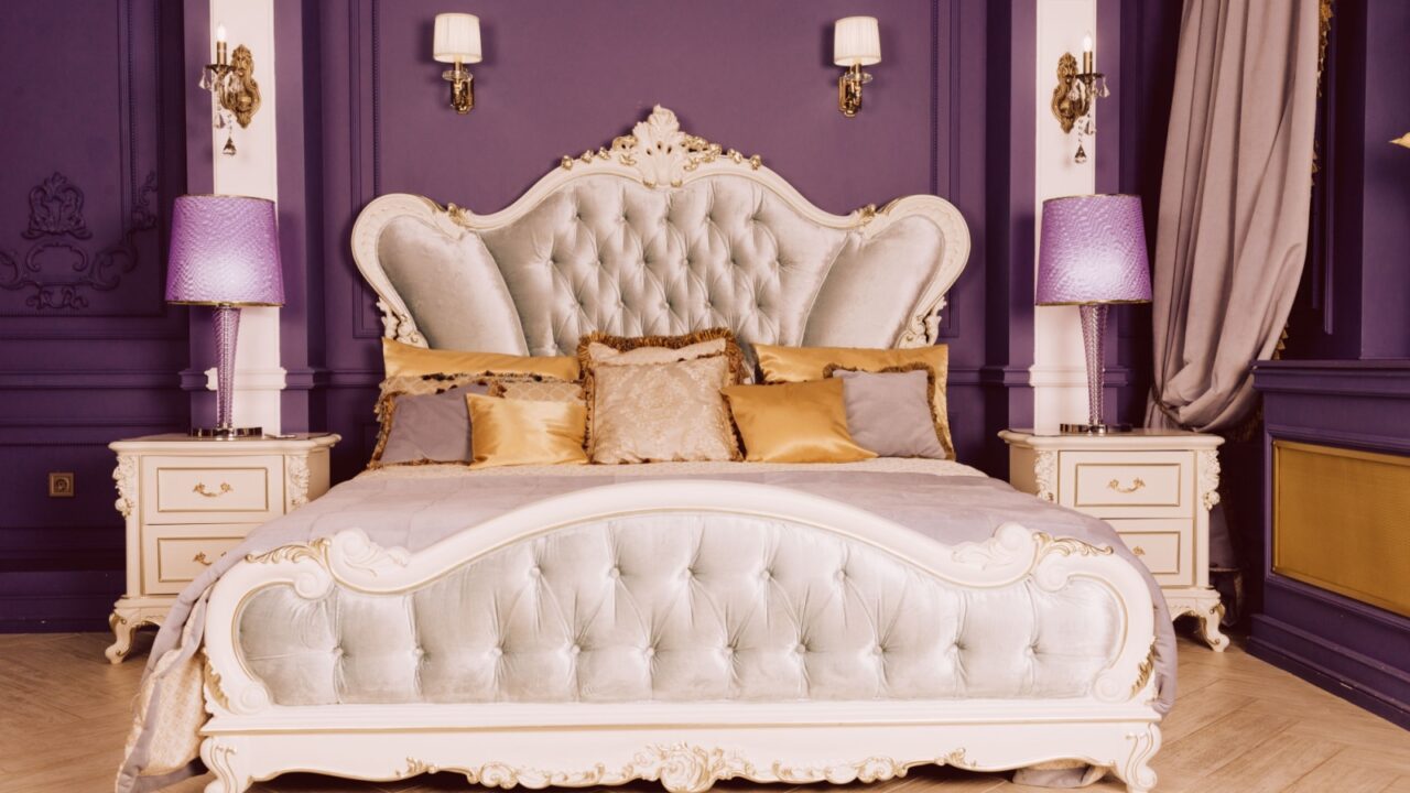 A luxurious bedroom with a large, ornate bed flanked by two nightstands and purple lamps.