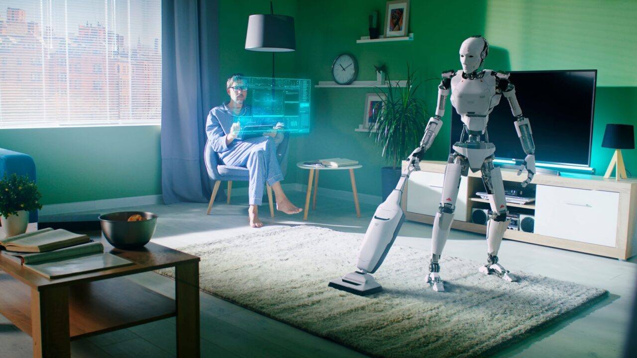 A person sits with a digital interface while a robot vacuum cleans the living room.