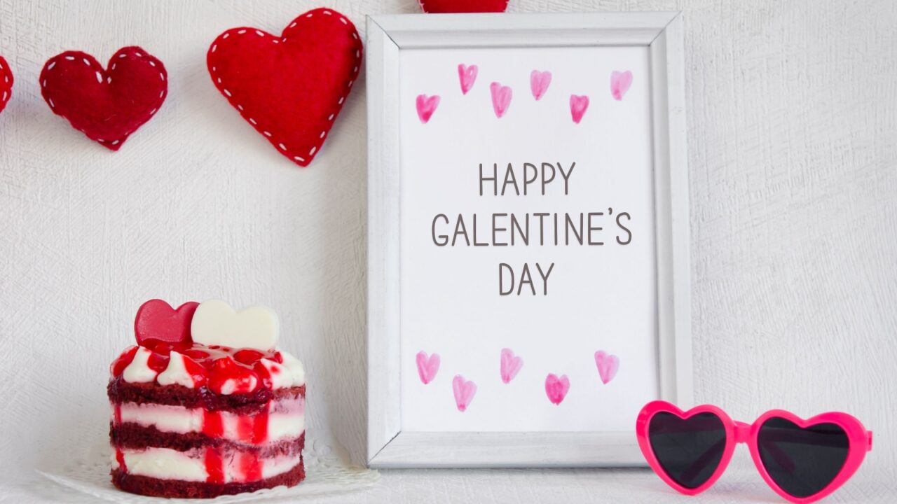 Celebratory display with a cake and a framed message saying "Happy Galentine's Day" surrounded by heart decorations.