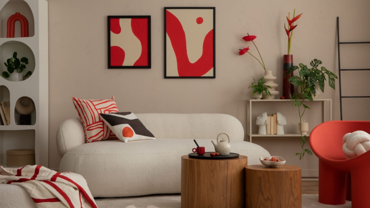 A stylish living room interior with a cozy white sofa, wooden coffee table, throw blanket, shelf, plants, and art frames on the wall.