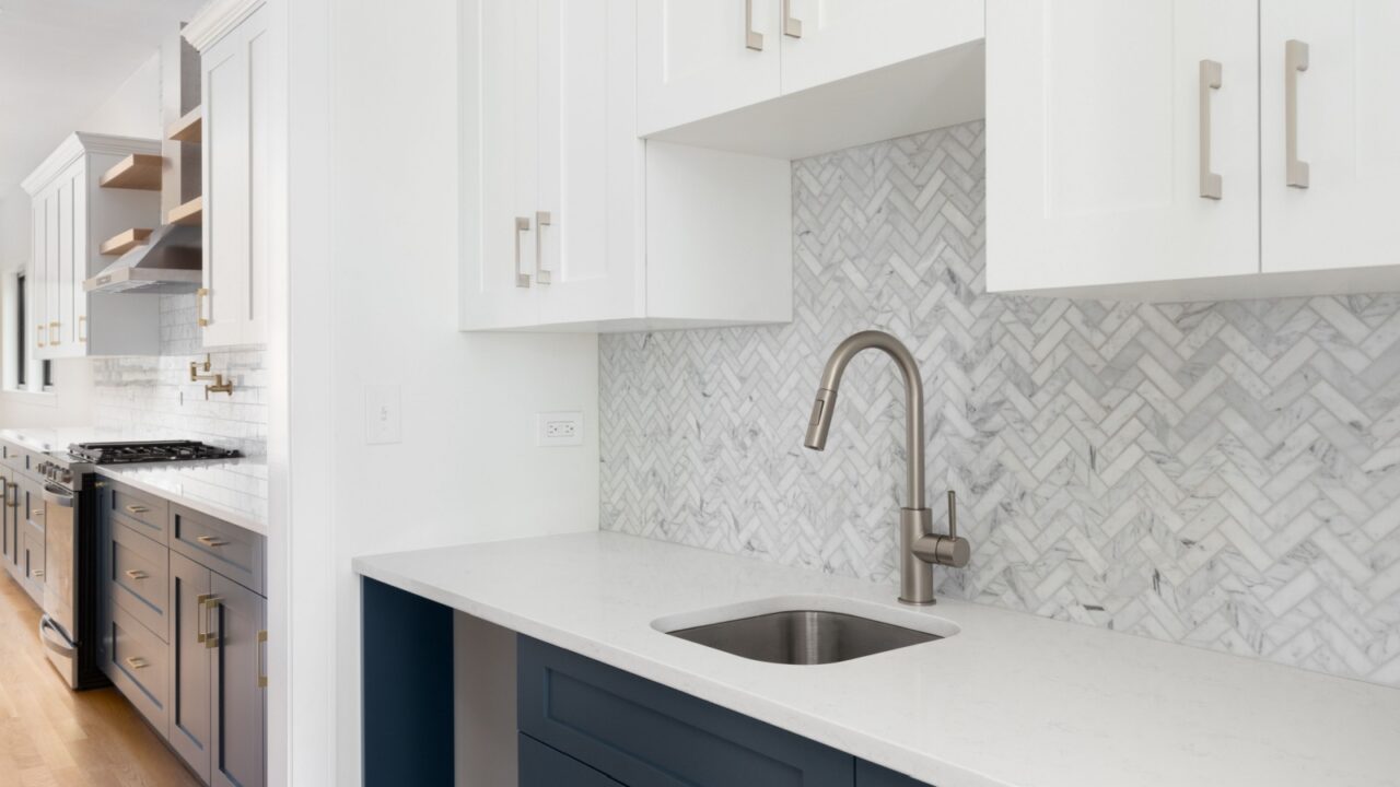 Stylish kitchen with a marble herringbone backsplash, white cabinets, and a contemporary faucet over a stainless steel sink.