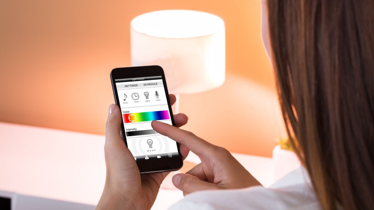 A woman using her smartphone to adjust the light of a smart lamp.