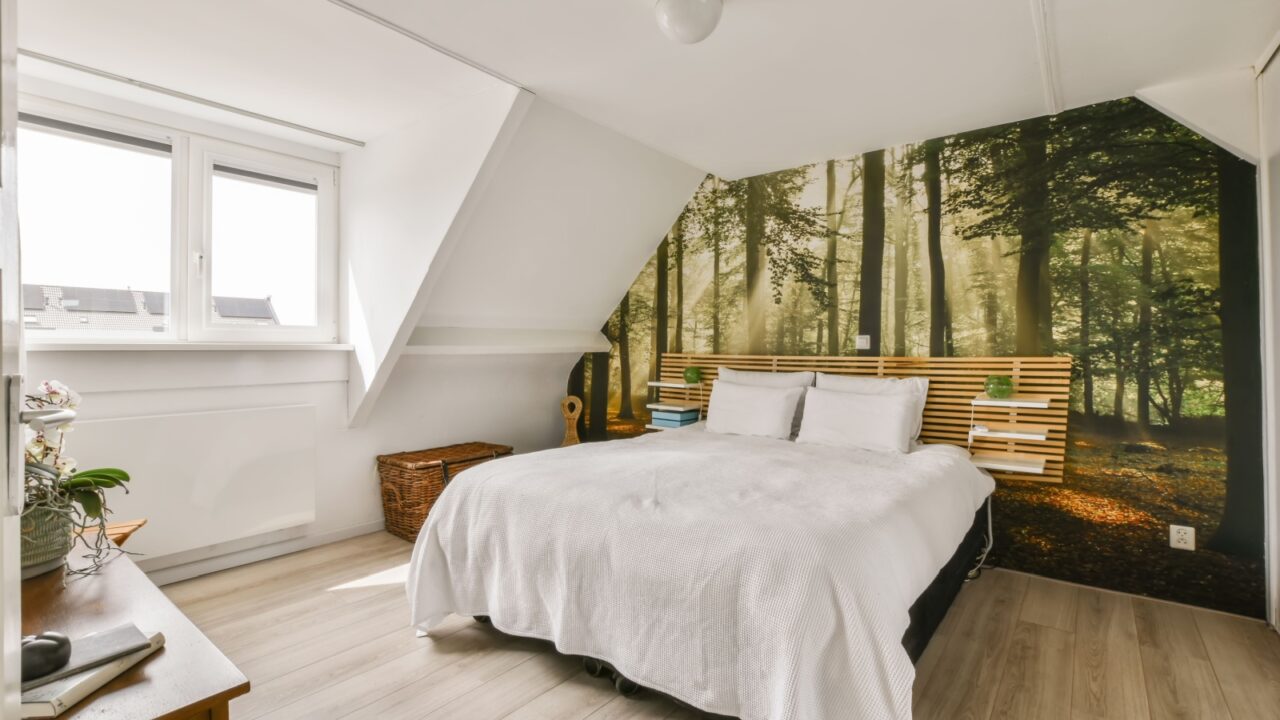 A modern bedroom interior with a cozy bed with wooden pallet headboard with shelves in front of a forest mural wall.