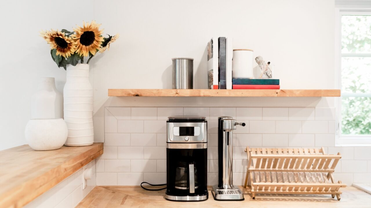 A coffee maker on a kitchen counter adorned with sunflowers in a vase and neatly arranged books.