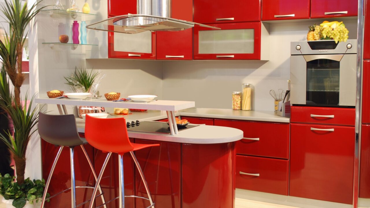 A modern kitchen with red cabinets and a breakfast bar with two stools.