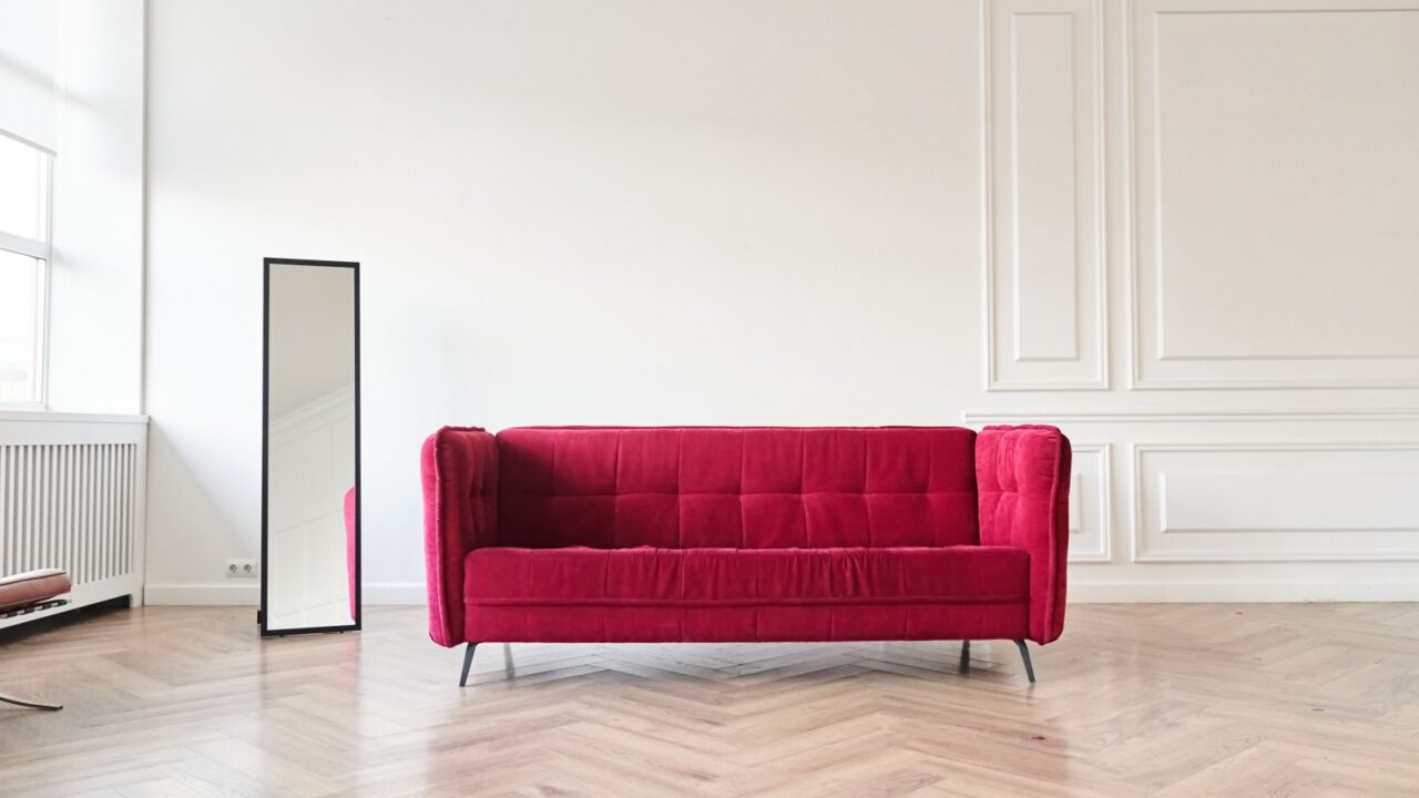 Minimalist room with red sofa and tall mirror.