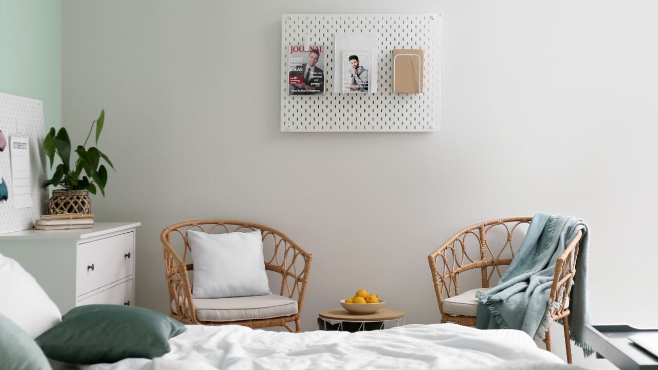 A stylish bedroom interior with a cozy bed, woven chairs, small potted plant, and a pegboard on the wall.