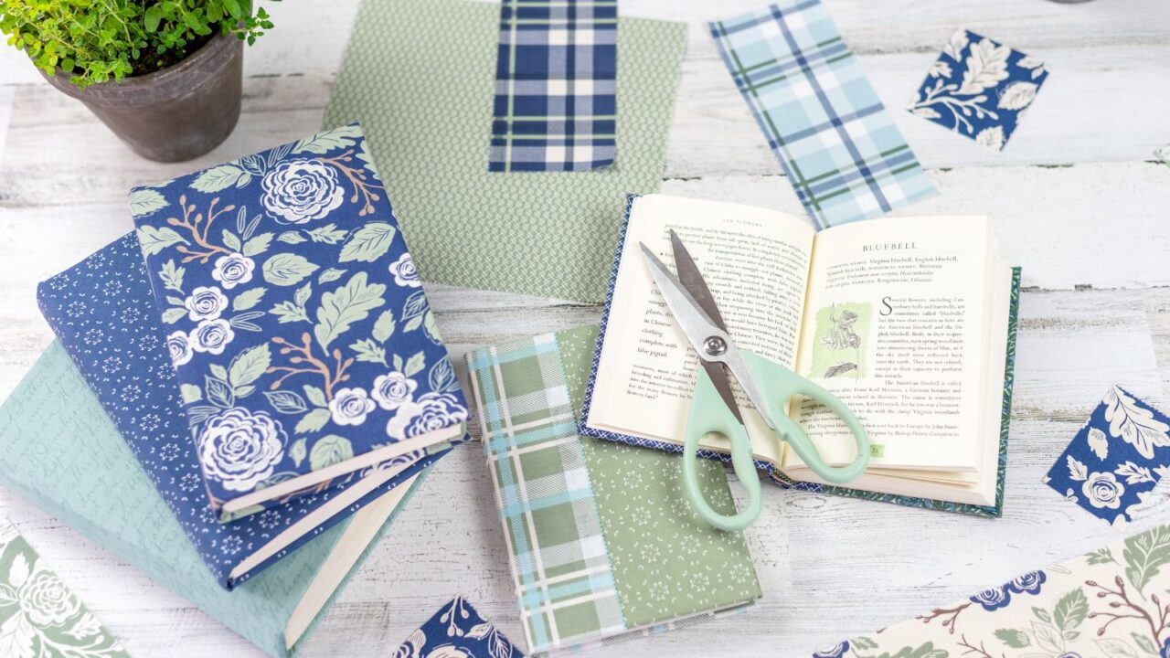 Books, printed paper sheets, potted plant, and a scissor on a wooden table.