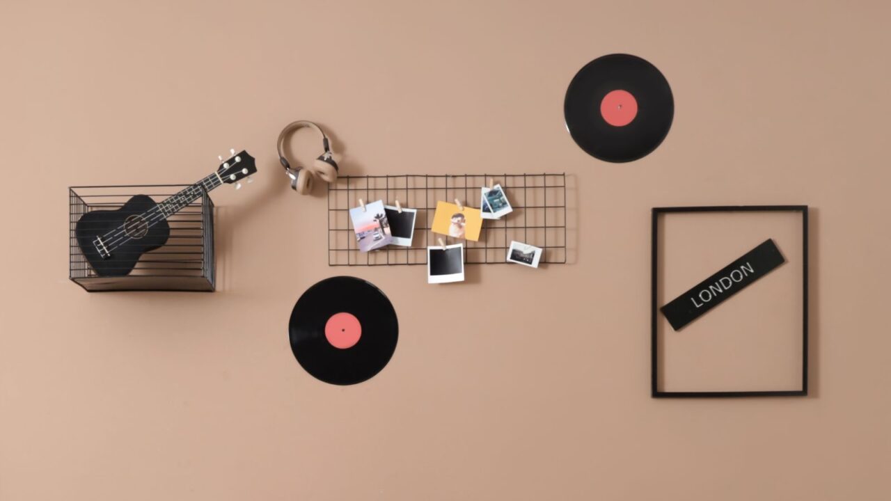 A coral wall featuring a mesh grid with polaroids, vinyl records, empty frame, headphones, and a mesh box with ukulele.