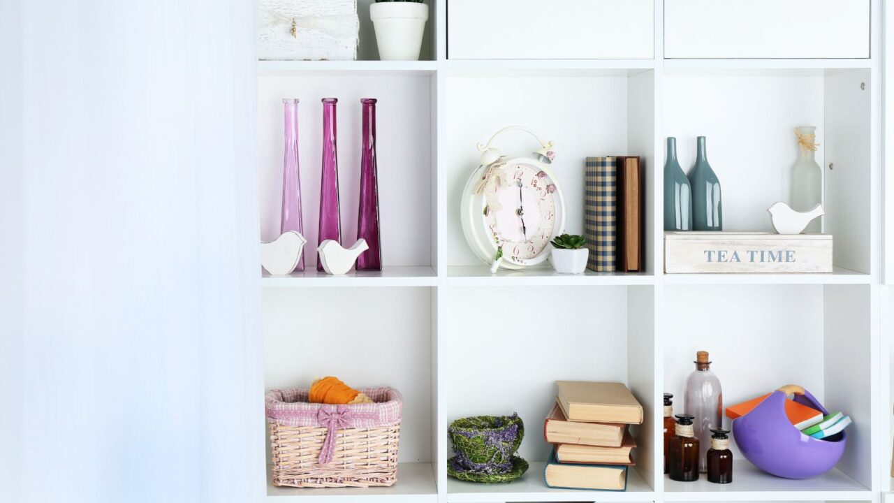 A white bookshelf with woven basket, clock, books, and decor accents.