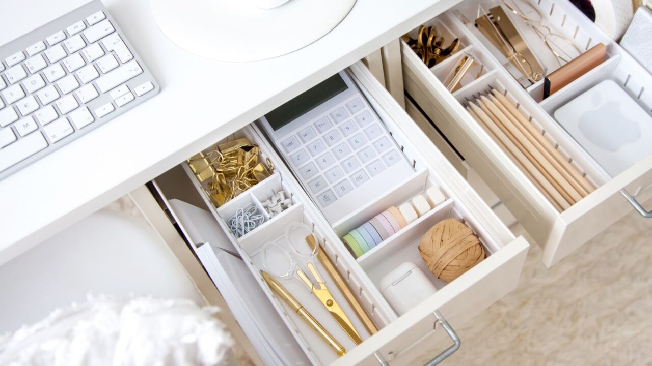 A white table with open drawers having drawer dividers holding stationery and accessories organized in it.