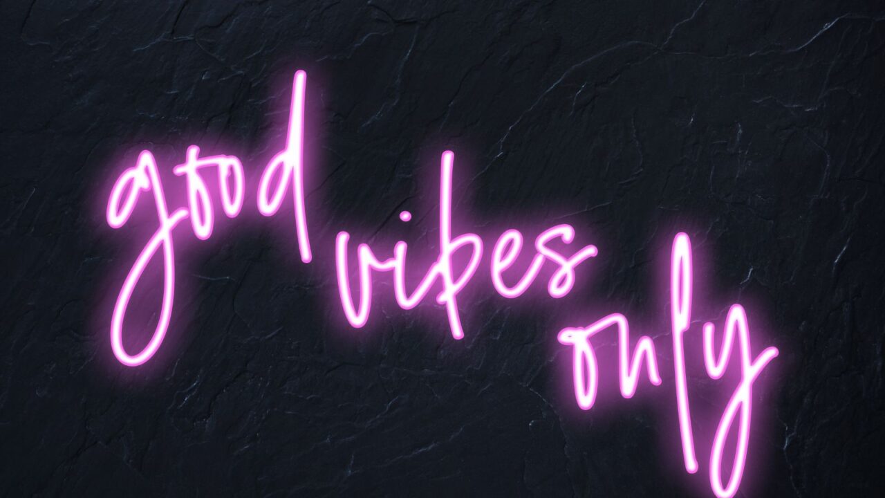 Pink neon sign saying "good vibes only" hanging on a black wall.