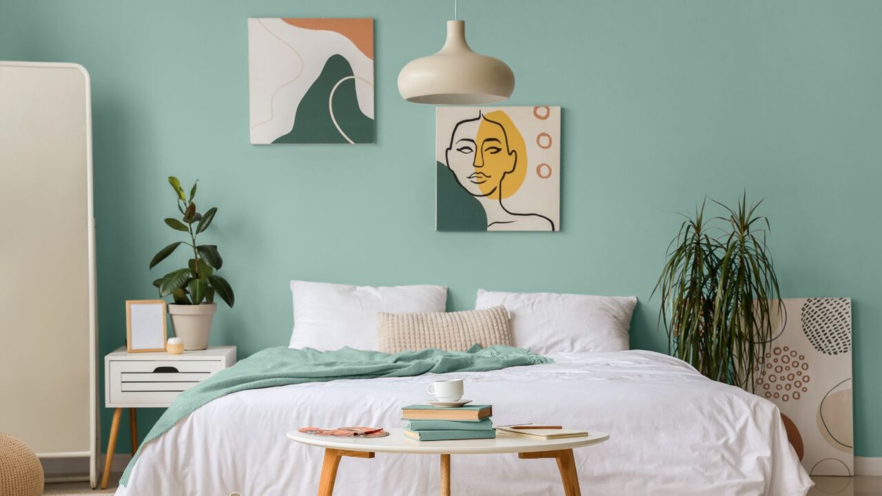 A modern bedroom with a green wall, bed, decorative plant, and wall art.