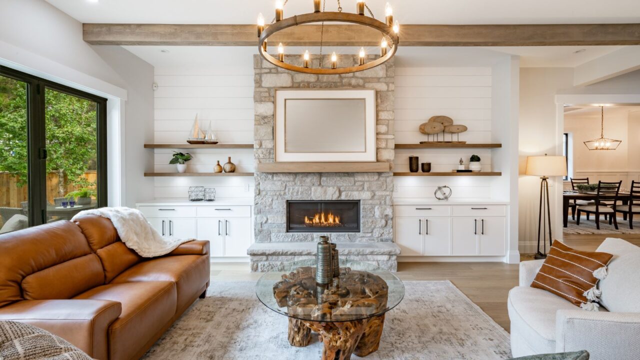 A living room interior with exposed wood beam, wheel chandelier, sofa, coffee table, and rug.