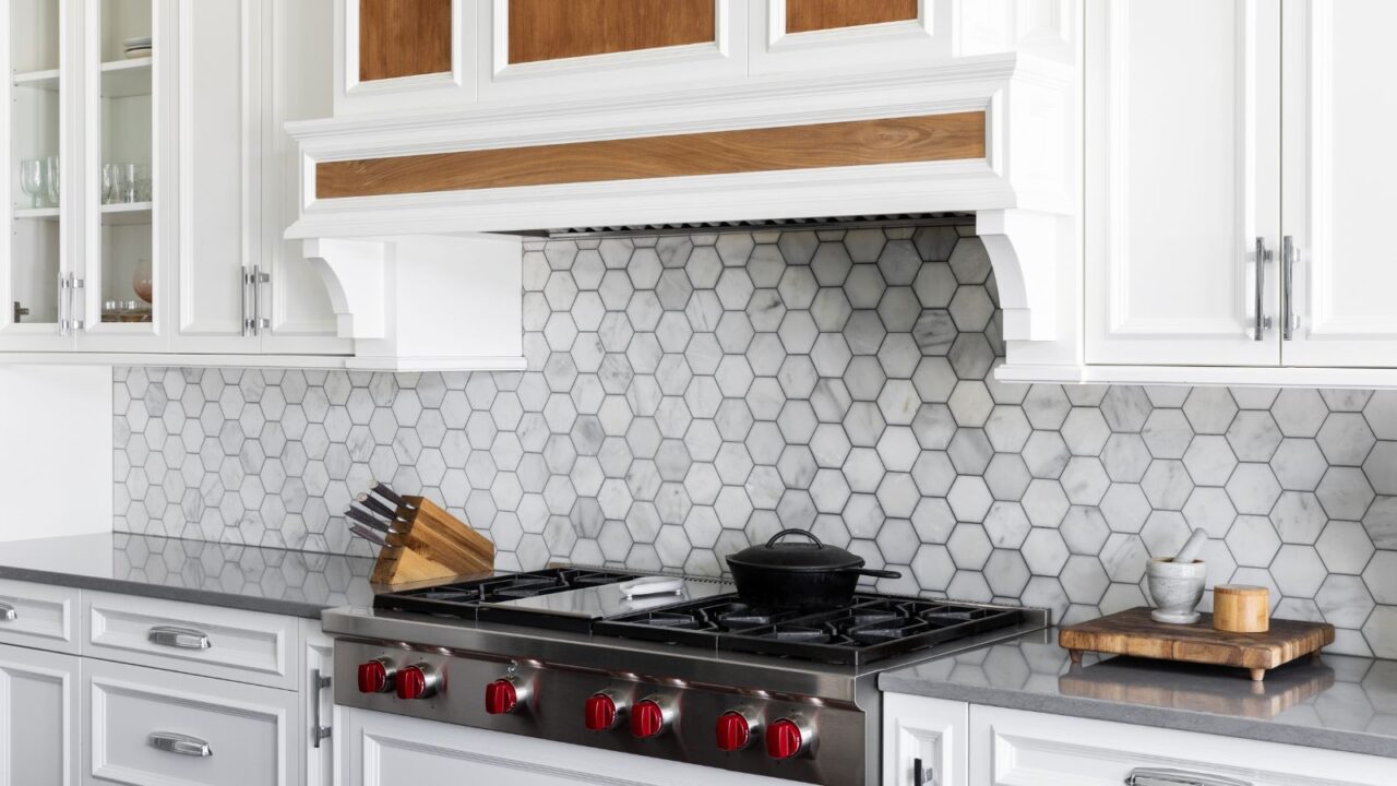 A kitchen interior with white cabinets, countertop, and hexagonal marble tiles backsplash.