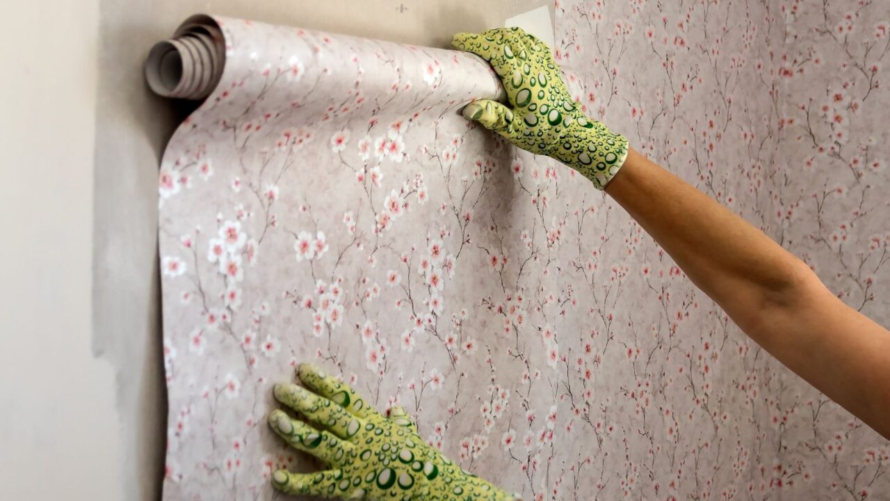 A person applying peel-and-stick wallpaper in floral pattern on a white wall.