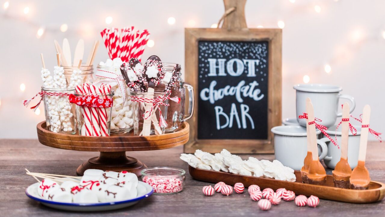 A hot chocolate station with different toppings and mugs on a wooden table.