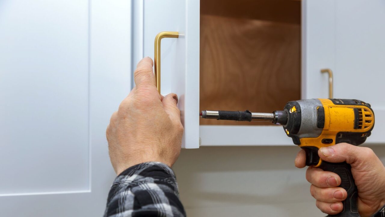 A man changing the handle of a white cabinet.