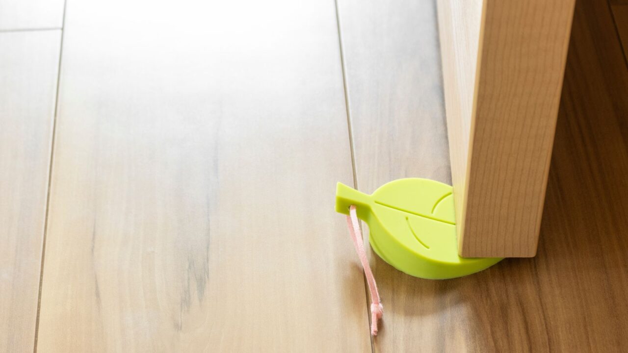 A wooden door held by a leaf-shaped doorstop.